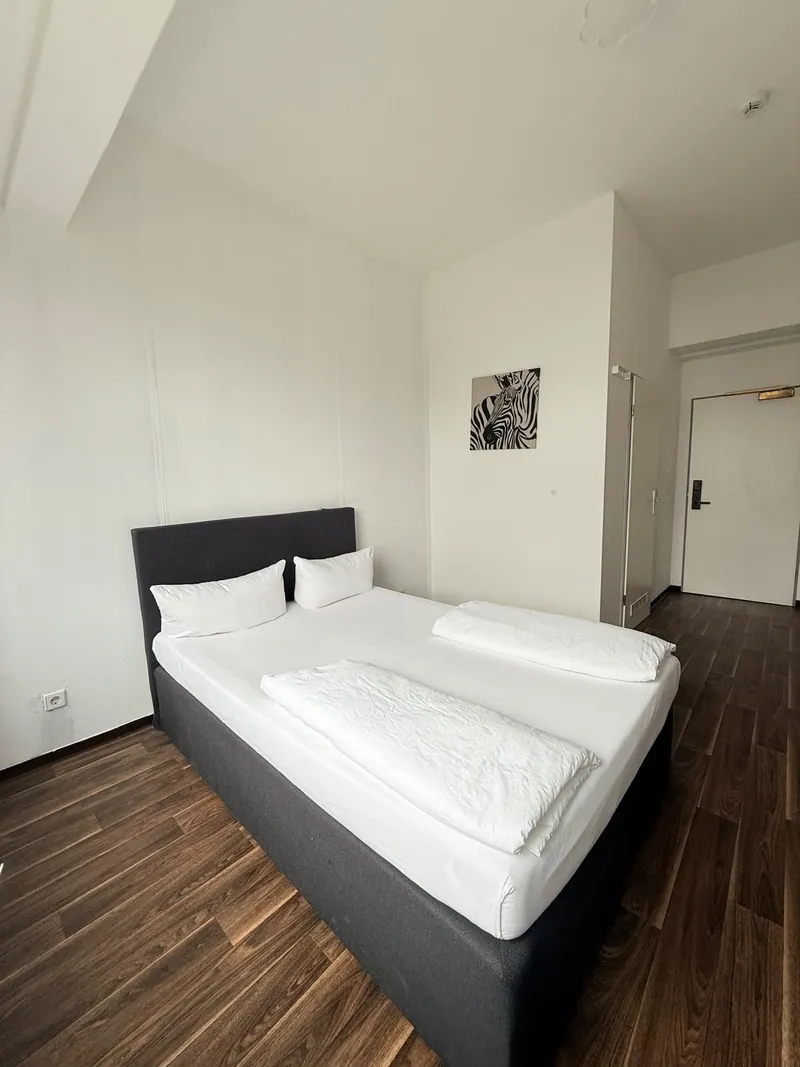 Originalaufnahme eines Ootel-Doppelbettzimmers mit dunklem Bett und Holzboden