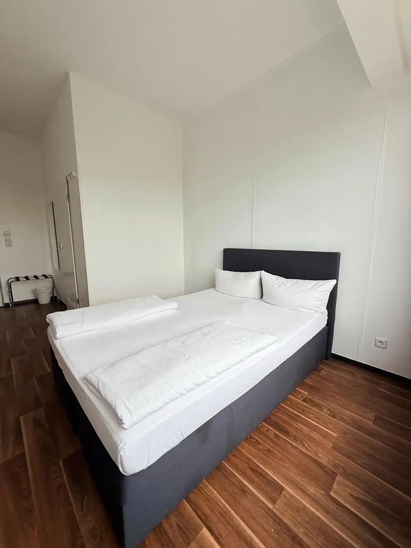 Originalfoto eines Ootel-Doppelbettzimmers mit dunklem Bett und weißer Bettwäsche